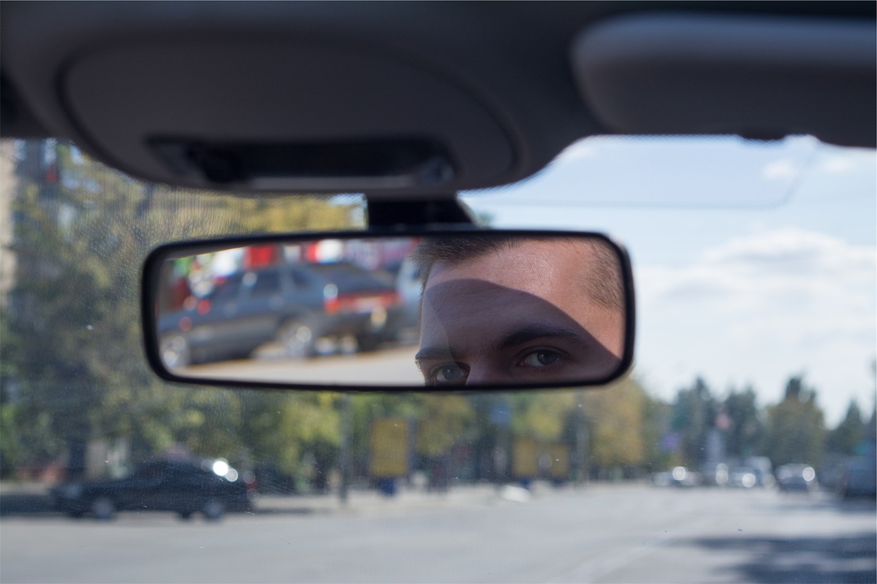 Ein Mann schaut beim Autofahren in den Rückspiegel.