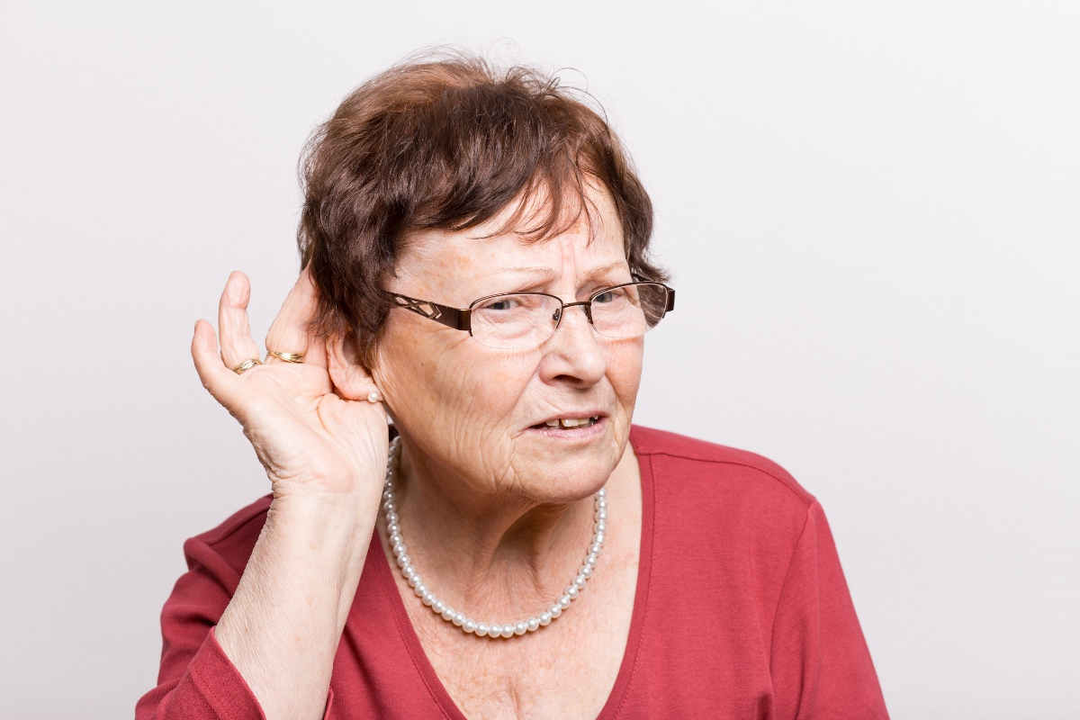 Eine schwerhörige Frau, hält sich die Hand vors Ohr, um besser hören zu können.