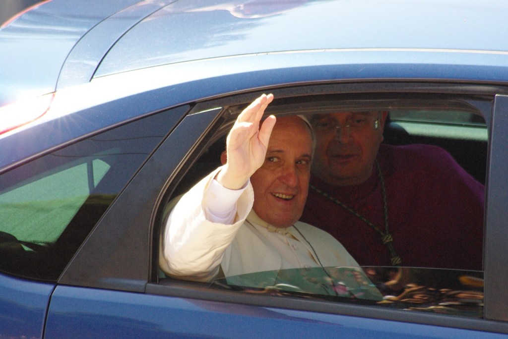 Der Papst sitzt in einem Auto und winkt aus dem Fenster.