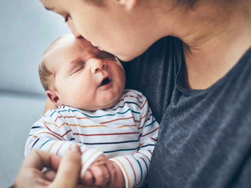 Eine Mutter küsst ihr neugeborenes Baby auf die Stirn.