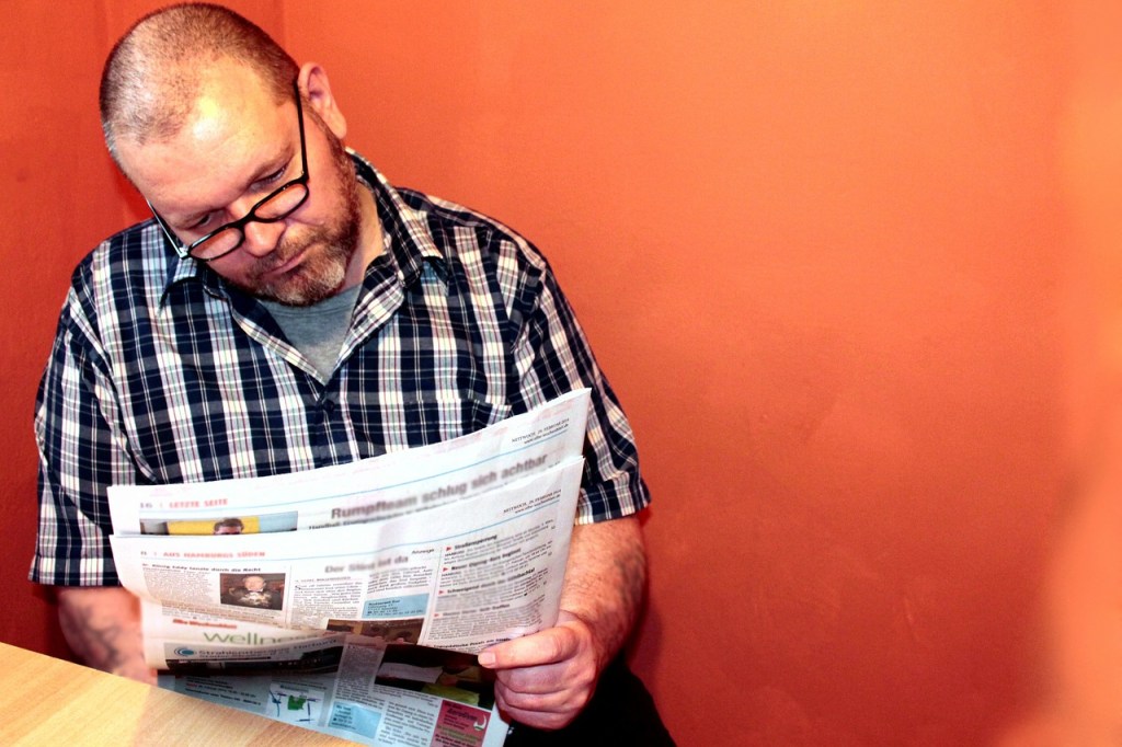 Ein Mann mit Brille und kariertem Hemd liest eine Zeitung.