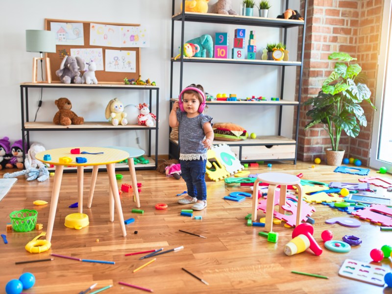 Ein kleines Mädchen steht in einem unordentlichen Kinderzimmer.