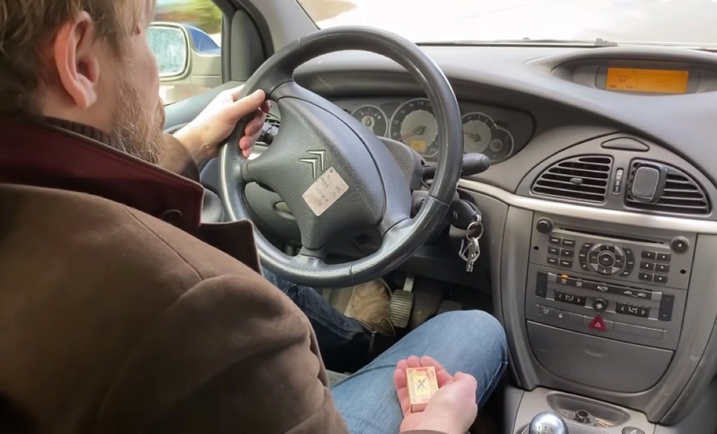 Ein Mann sitzt in seinem Auto und hält eine Streichholzschachtel in der Hand.