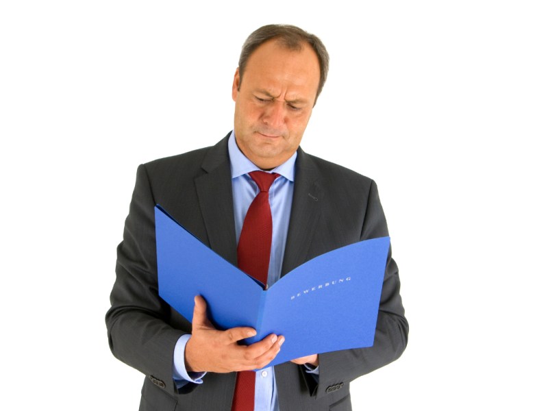 Ein Mann in einem Anzug mustert skeptisch eine Bewerbungsmappe.
