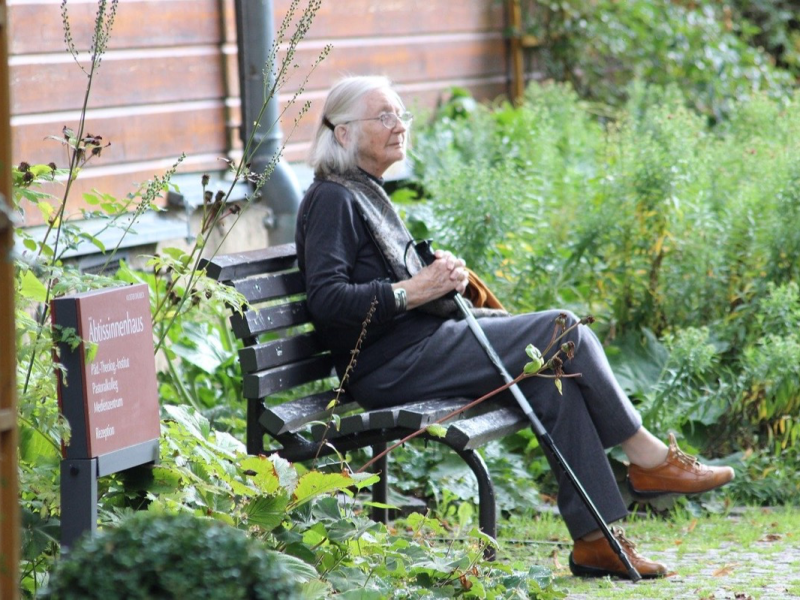 Eine alte Frau sitzt auf einer Parkbank.