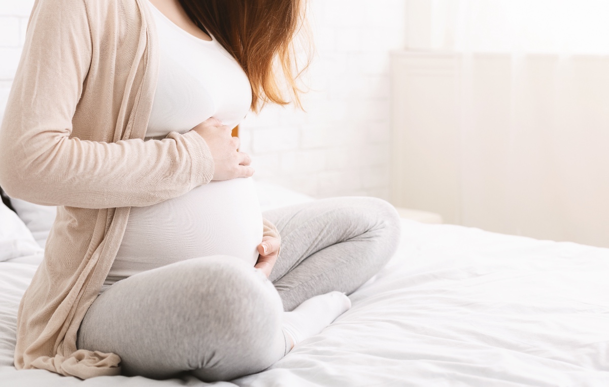 Eine werdende Mutter sitzt auf einem Bett und hält sich den Bauch.