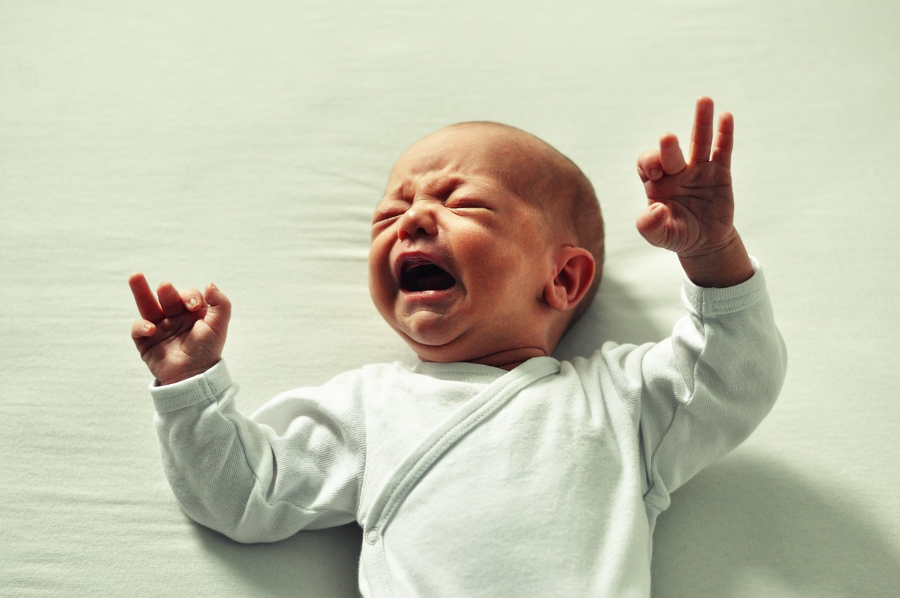 Ein Baby im Strampelanzug liegt auf dem Rücken und schreit.